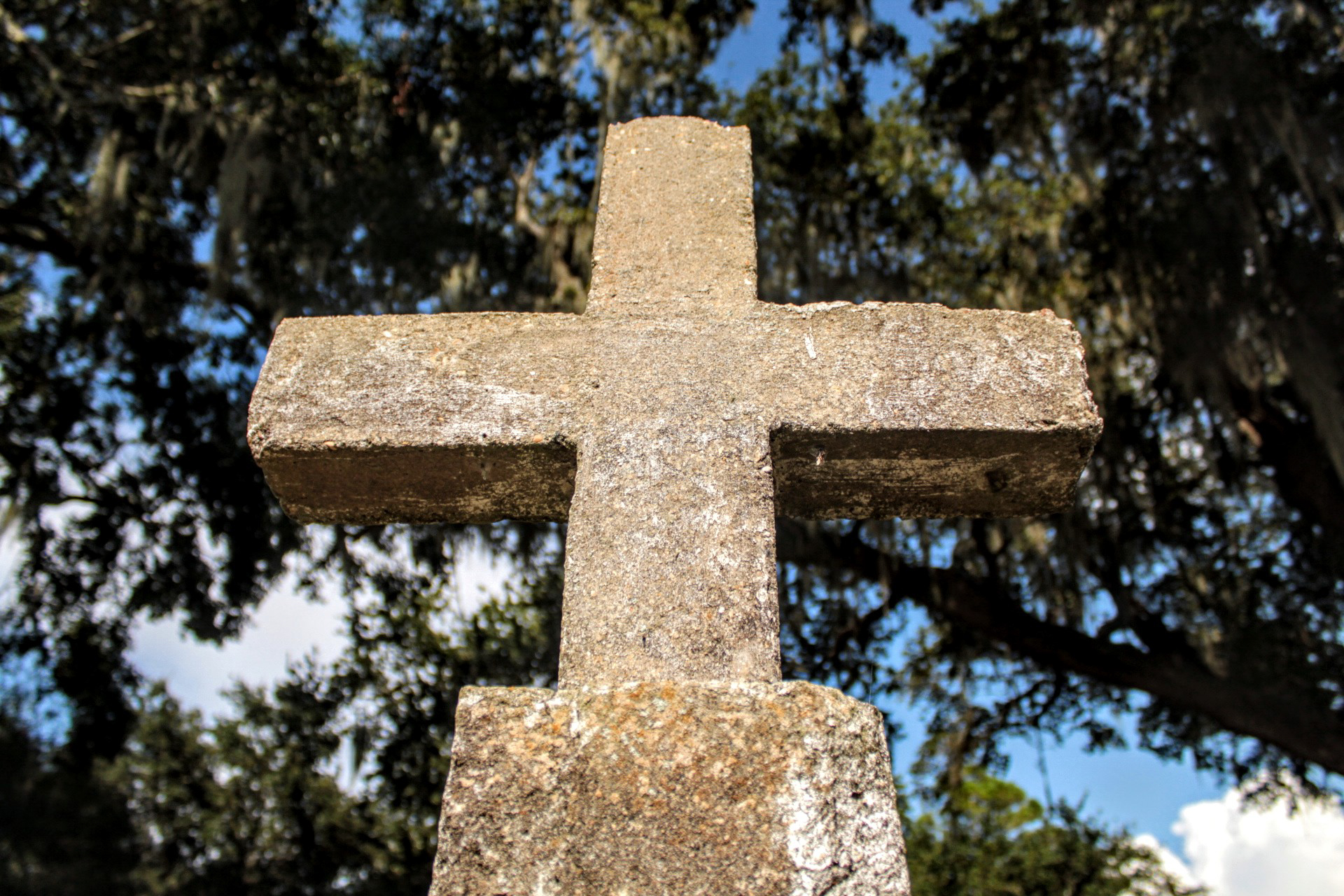 A standing concrete cross framed by oak trees and Spanish moss.