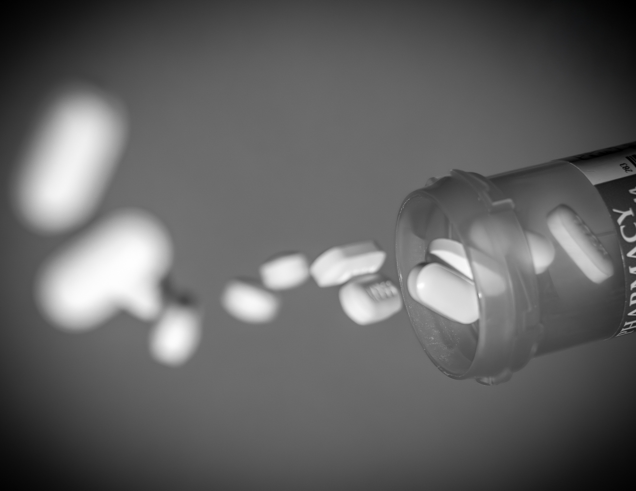 Prescription medication spilling from an open bottle in black and white.